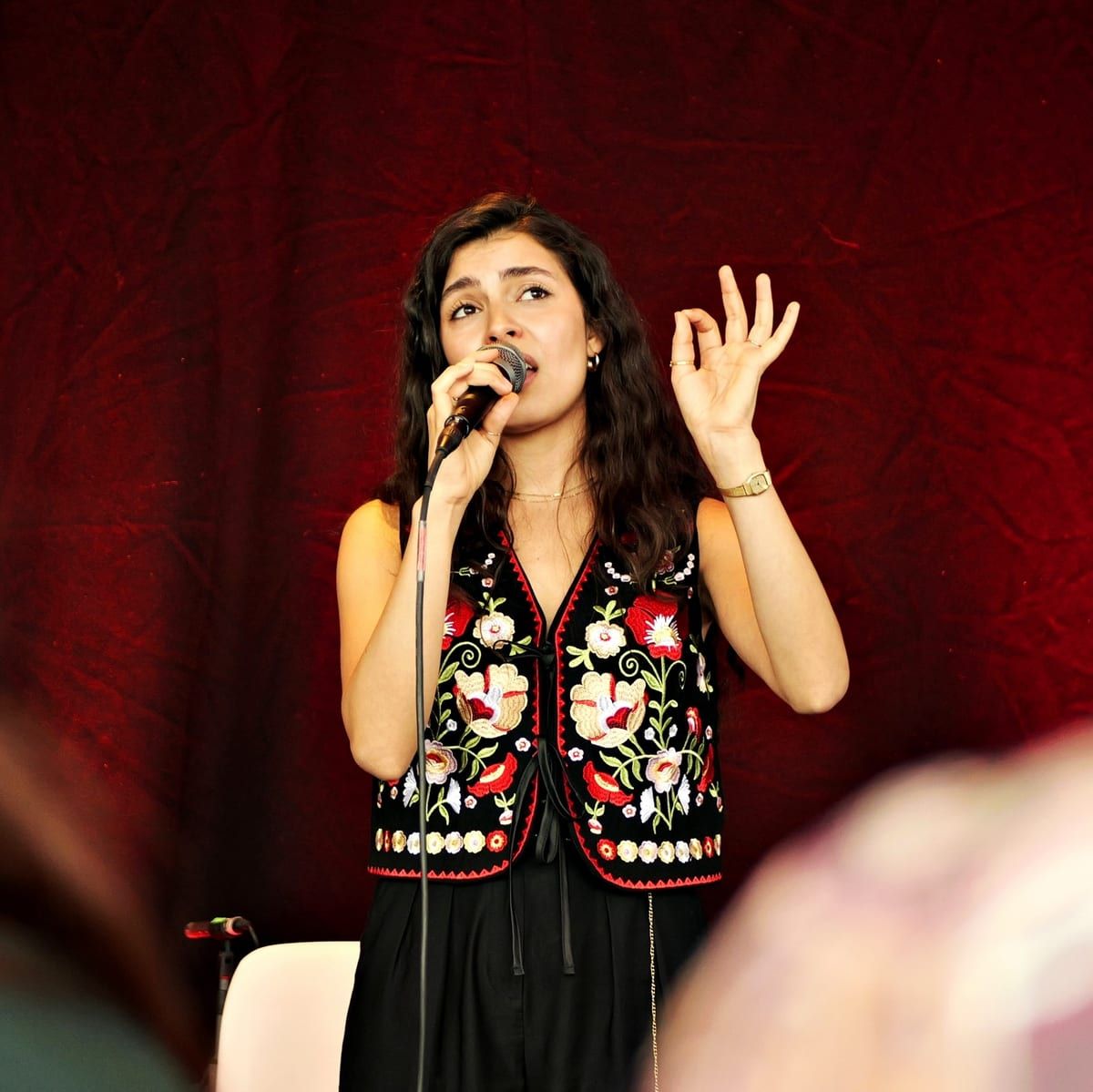 Olivia Mihet wearing a traditional Romanian embroidered vest against a crimson velvet backdrop