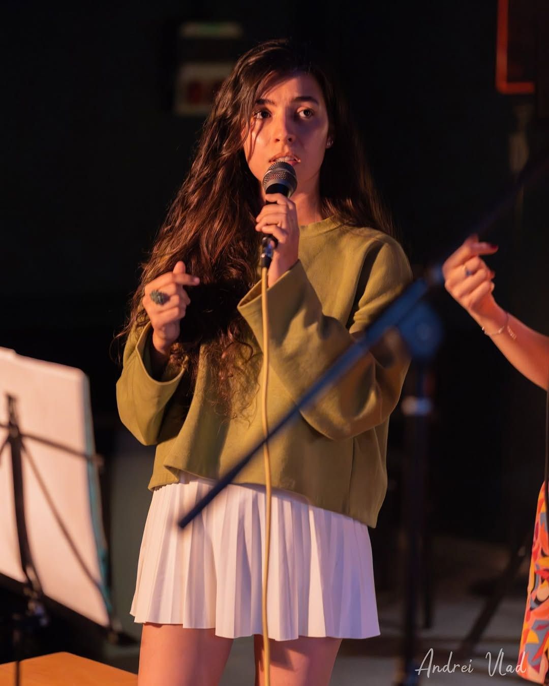 Olivia Mihet singing into a microphone in a green sweater under warm stage lighting