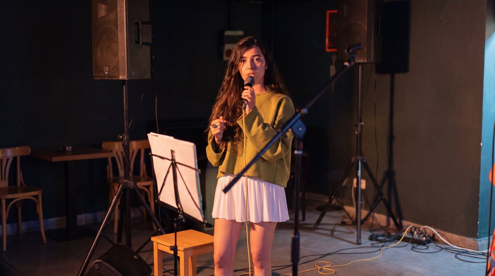 Olivia Mihet singing into a microphone in a green sweater under warm stage lighting