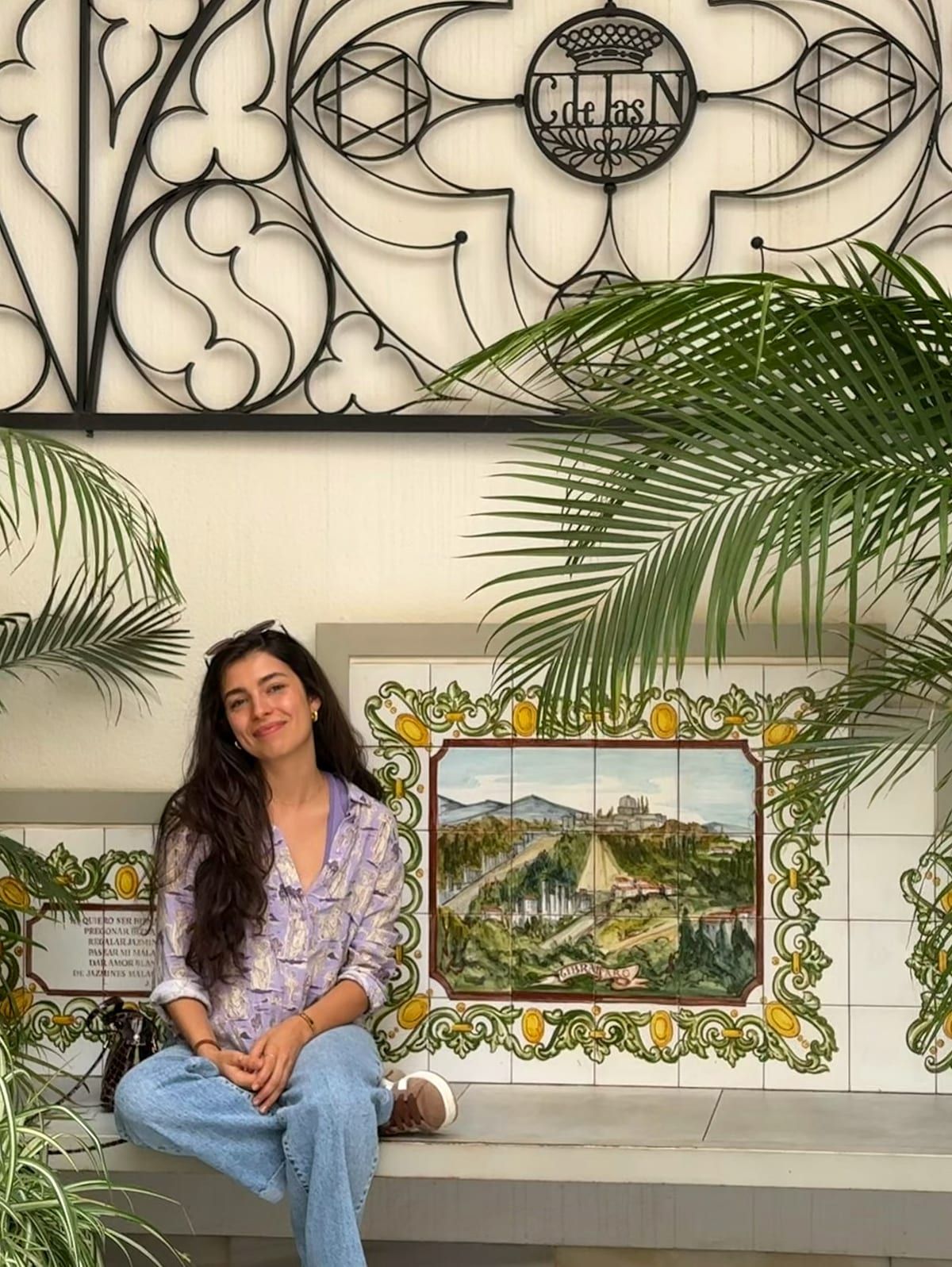 Olivia Mihet seated beside Andalusian-style patterned tiles with palm trees in the background
