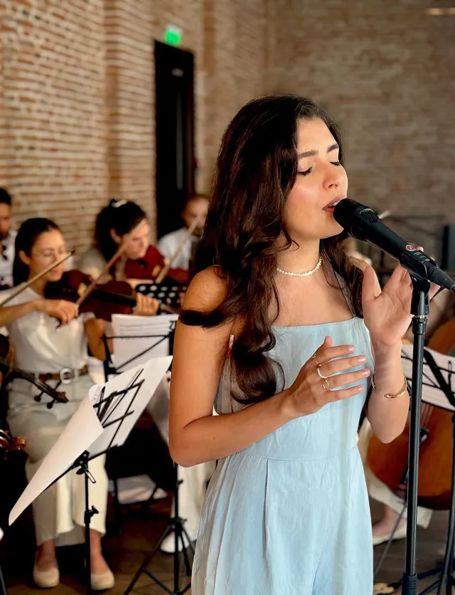 Close portrait of Olivia Mihet singing with eyes closed, violinists visible behind her at the same concert