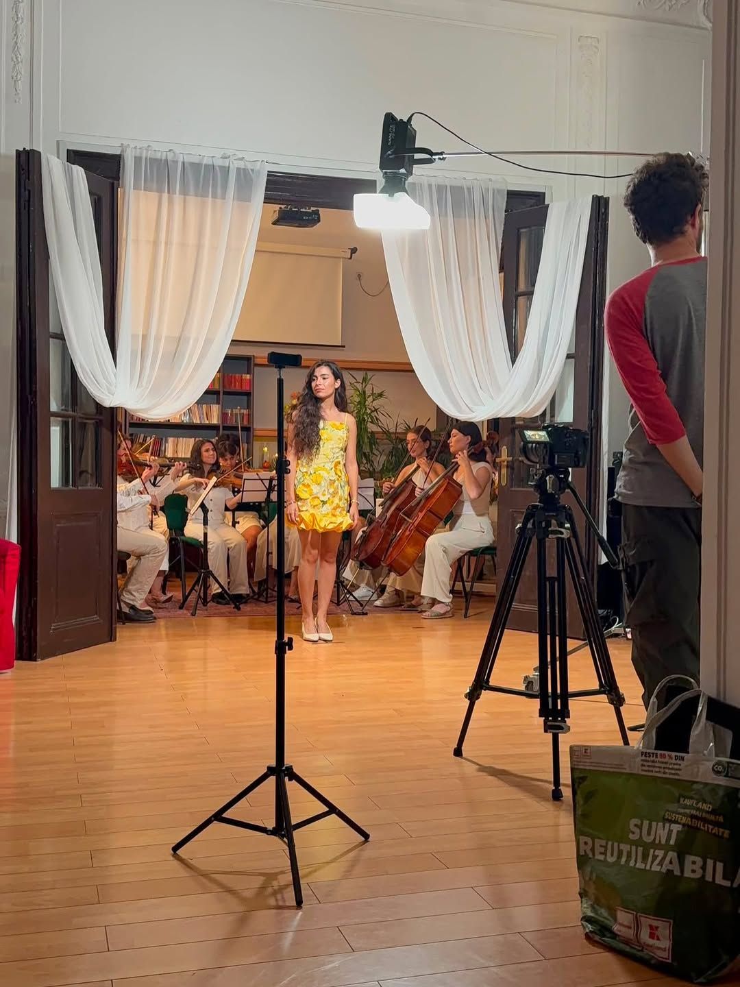 Behind-the-scenes shot of a video shoot with camera rig, Olivia in the yellow floral dress in the background